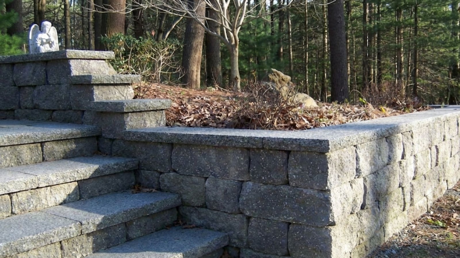 Granite retaining wall with built-in steps in wooded residential landscape