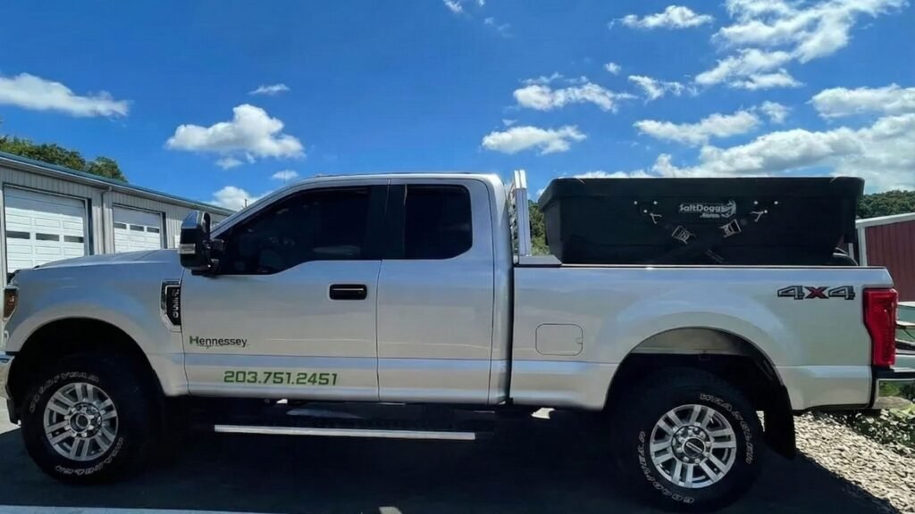 White Hennessey 4x4 work truck parked in a lot with a SaltDogg spreader in the truck bed on a sunny day
