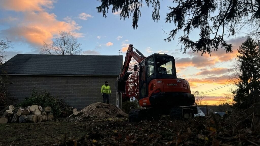 Excavator and operator completing residential tree removal at sunset in Seymour Connecticut